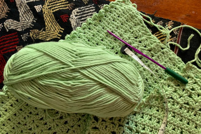 green crochet sweater with yarn, needle and measuring tape